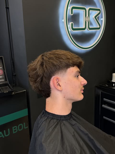 Coupe taper avec frange texturée, vue de profil devant l’enseigne du salon