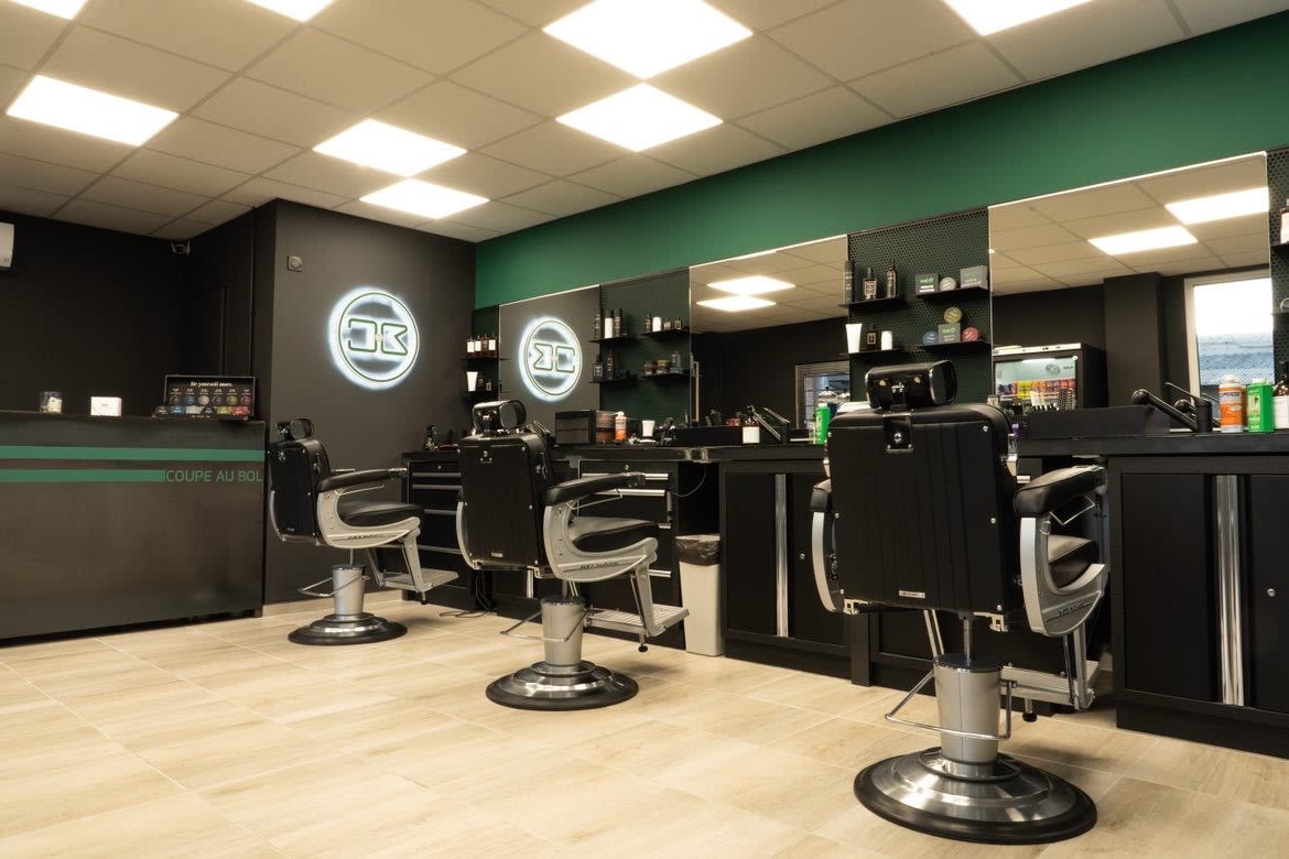 Intérieur du salon Coupe au Bol : trois fauteuils de barbier chromés face aux miroirs, enseigne lumineuse au mur