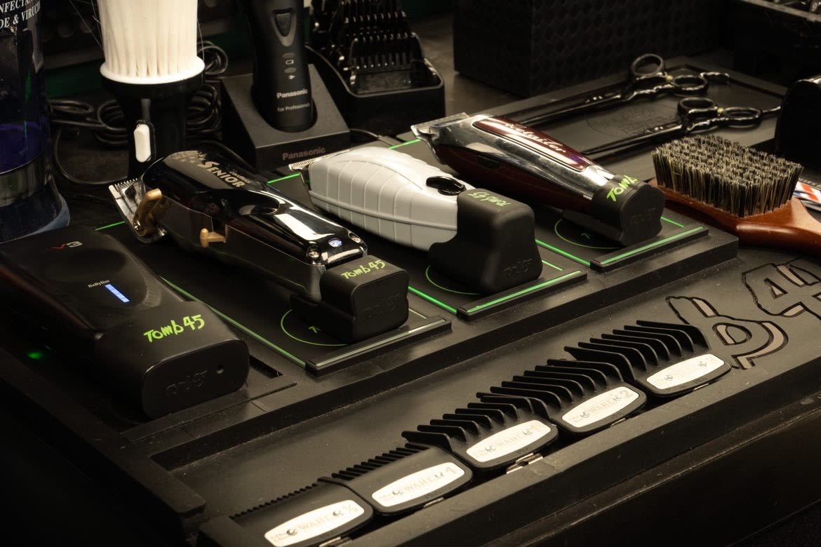 Plan de travail du barbier : tondeuses Wahl, Panasonic et BaByliss sur leur station de charge, ciseaux et brosse